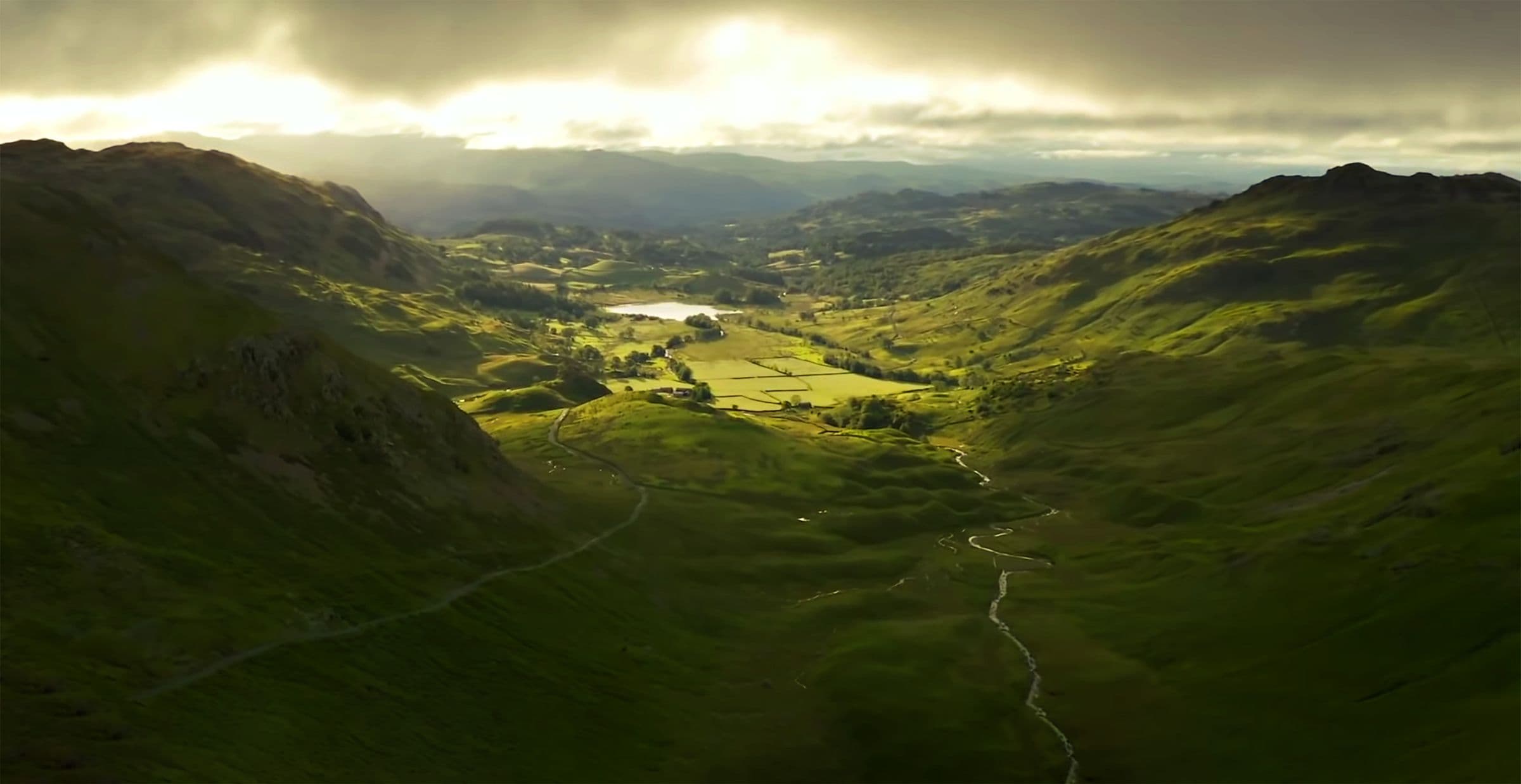 Dramatic aerial view over a green valley with sunlight breaking through clouds