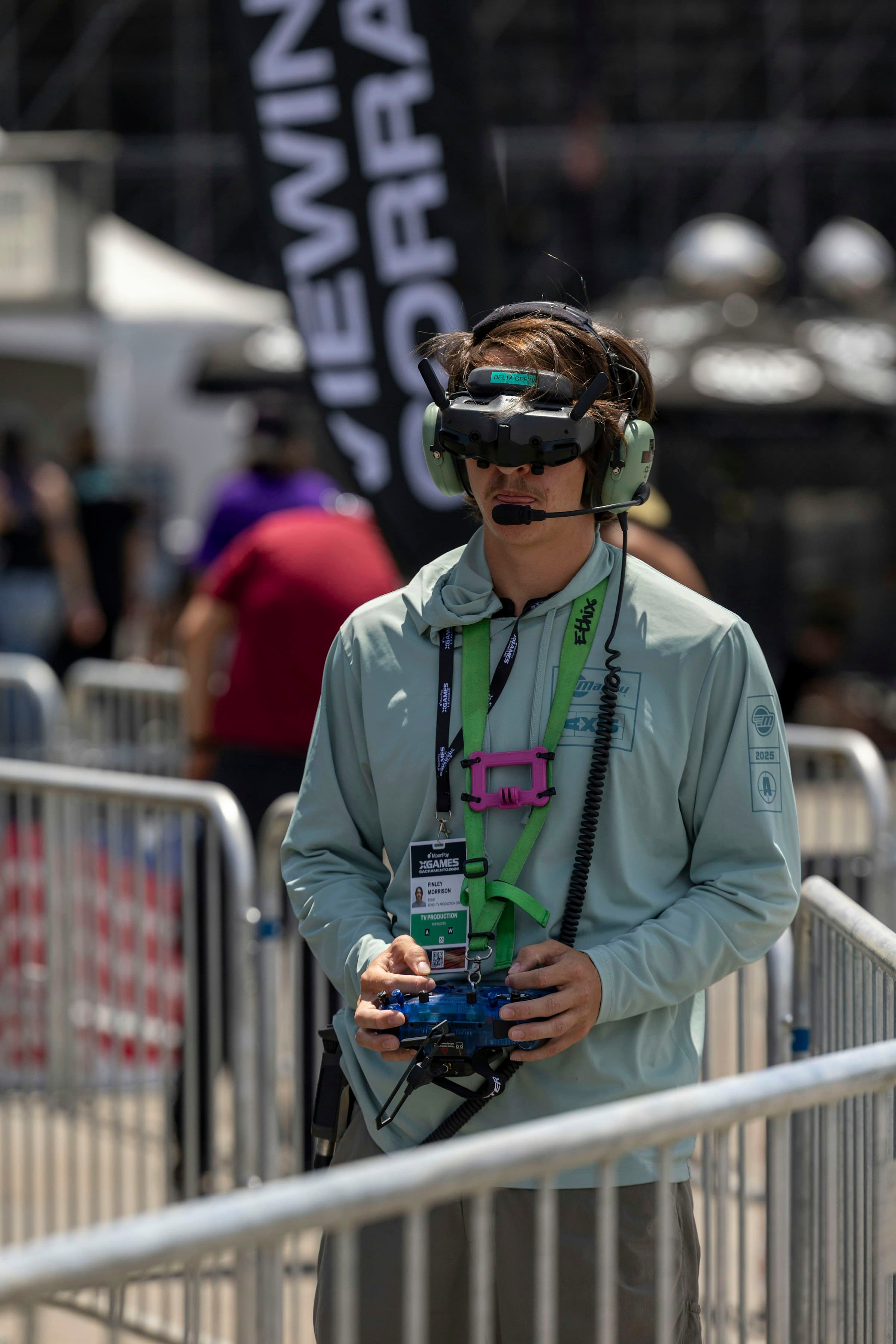 Close portrait of a pilot wearing FPV goggles and holding a transmitter at an outdoor event