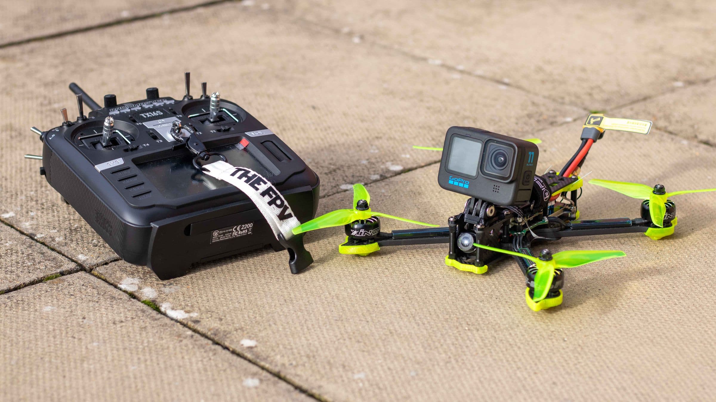 Close-up of a real FPV freestyle quadcopter with four arms and motors next to its radio transmitter